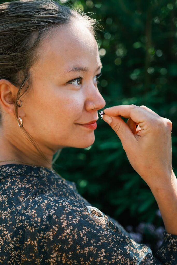 Sandra Lindström håller ett mörkt bär nära näsan, stående utomhus med grönska i bakgrunden.