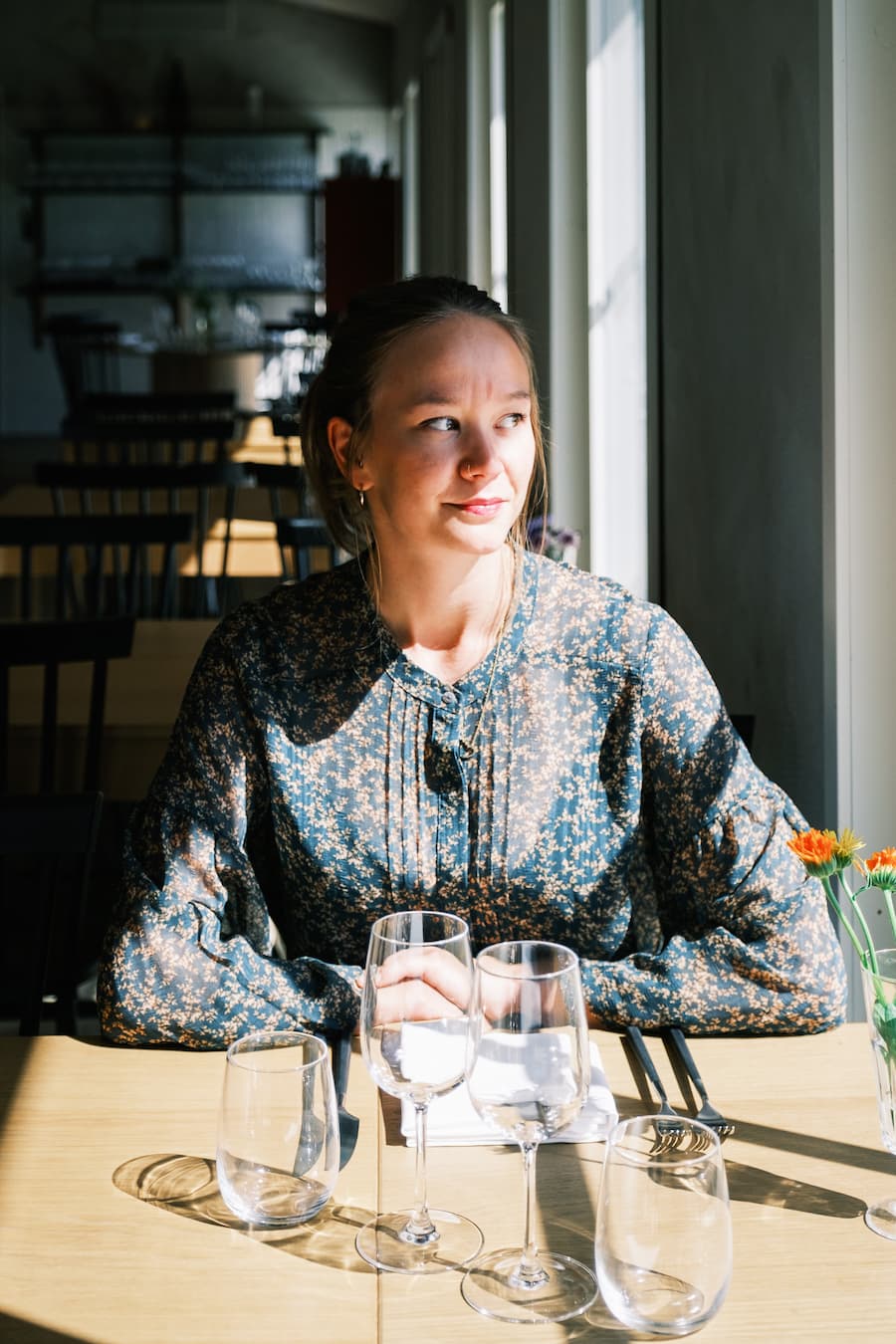 Sandra Lindström  ensam vid Back Pokets bord med tomma glas och blickar ut genom ett solbelyst fönster på en restaurang.